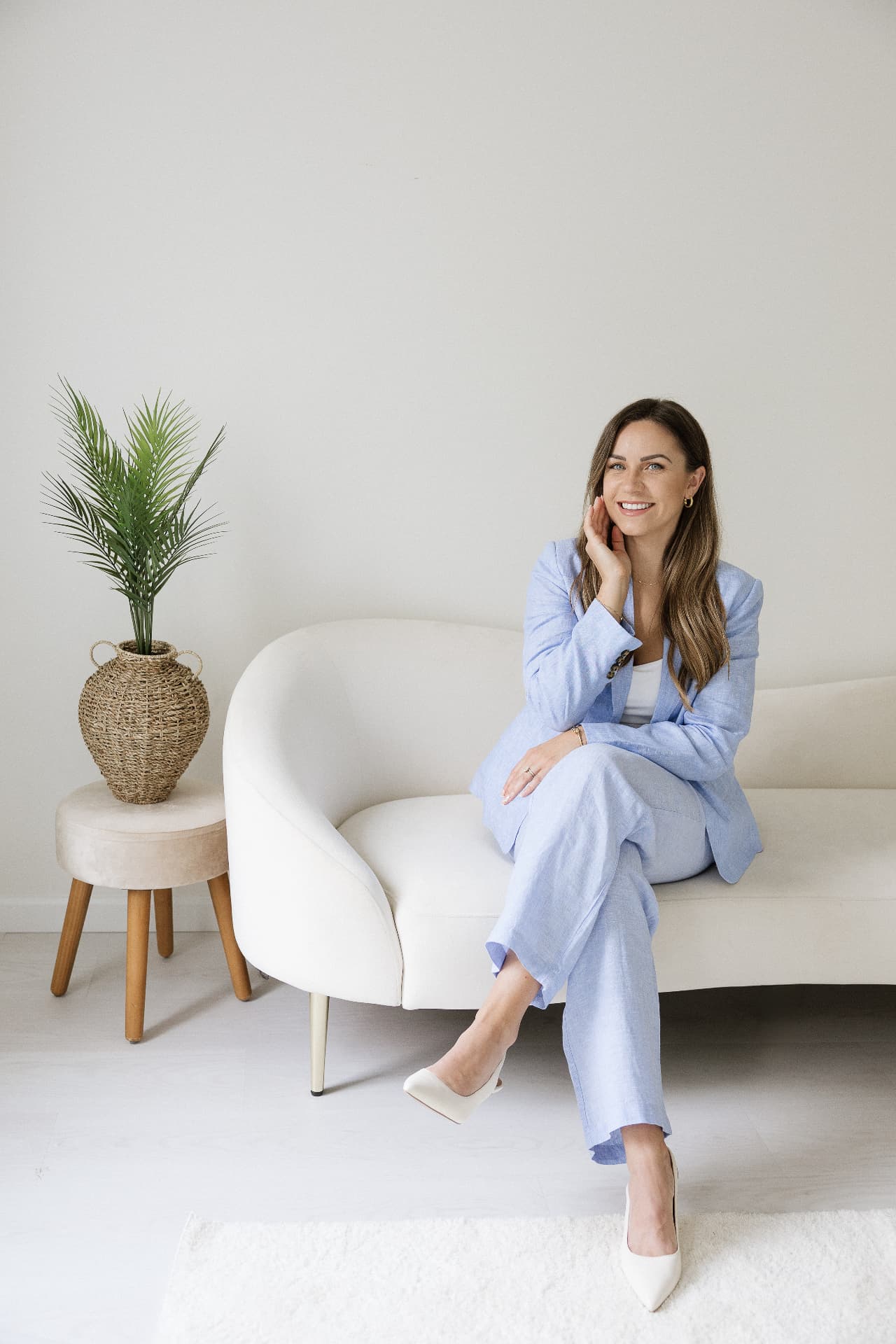 Alyssa seated on a cream sofa in a light blue linen suit beside a palm